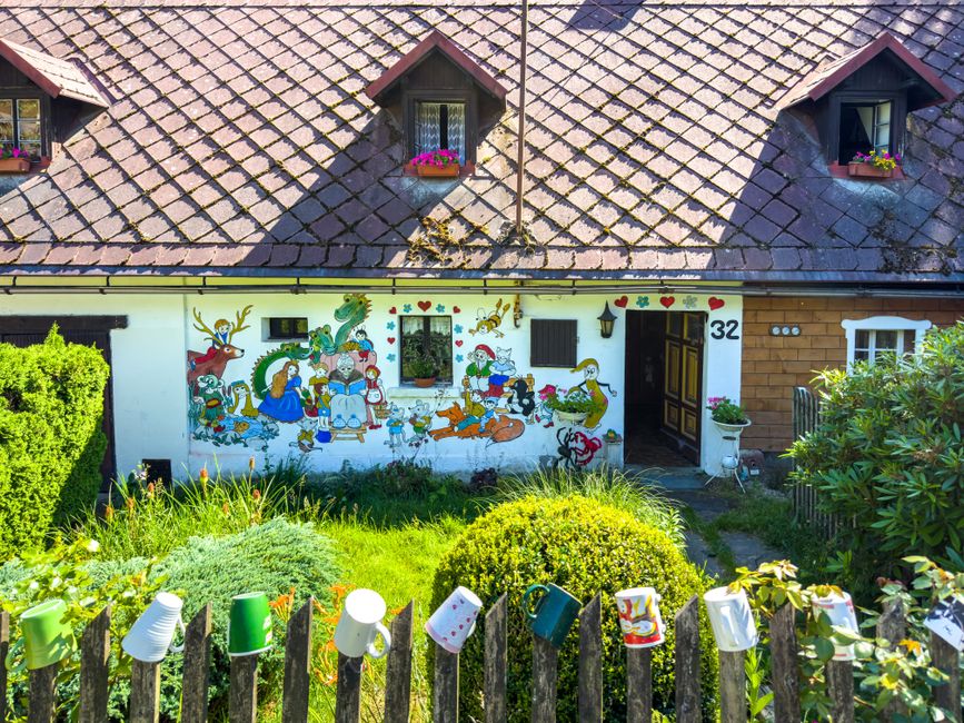 Small cottage with a painted mural wall and flowers in the front yard.